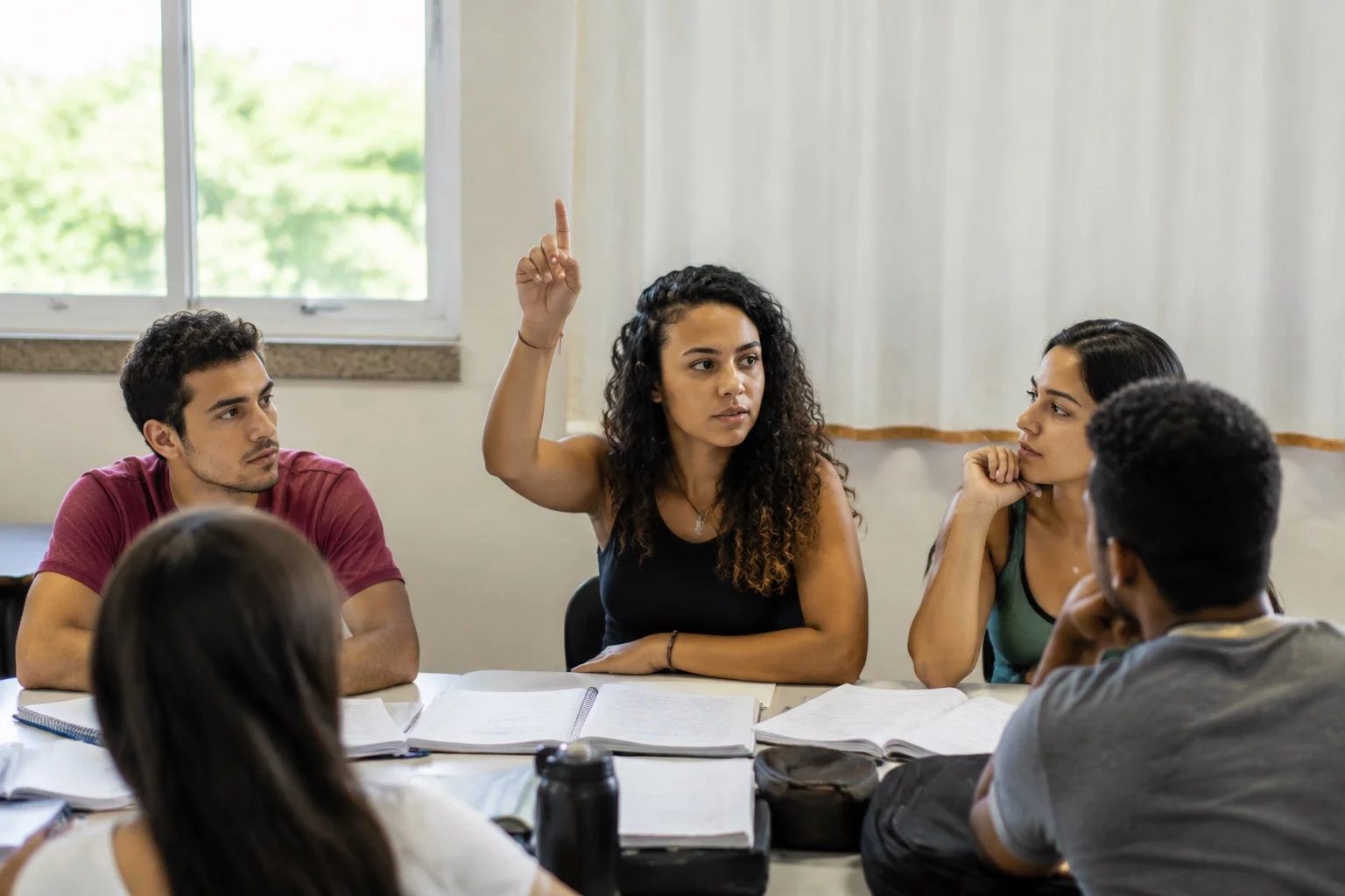 Estudante levantando a mão em uma mesa de seminário coberta de anotações
